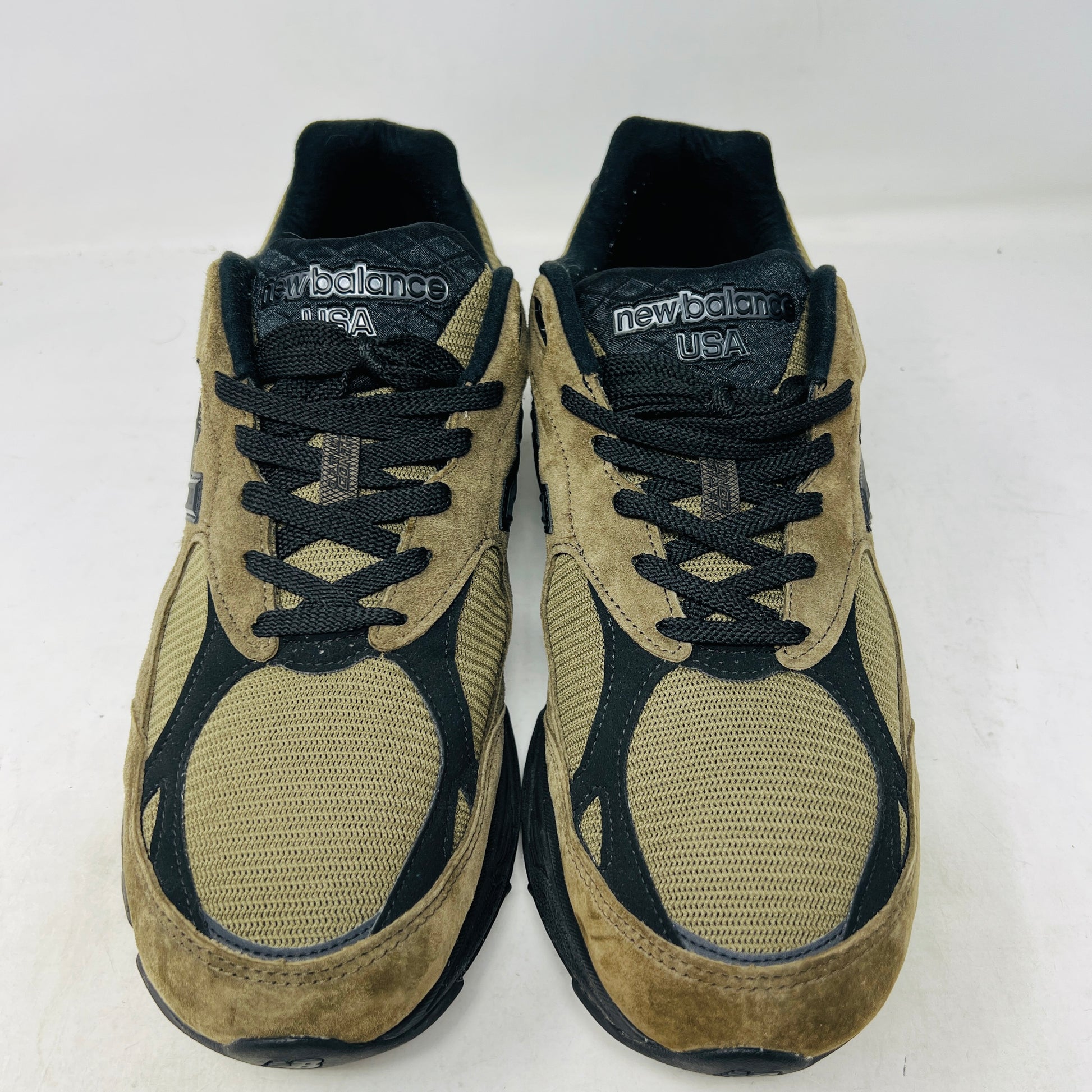 The New Balance 990v3 MiUSA JJJJound Brown Black athletic shoe, released in 2022, features tan and black mesh-suede uppers with an N logo on the side and 990 on the heel. It sits atop a black shoebox with the label M990JJ3 and shows light wear.