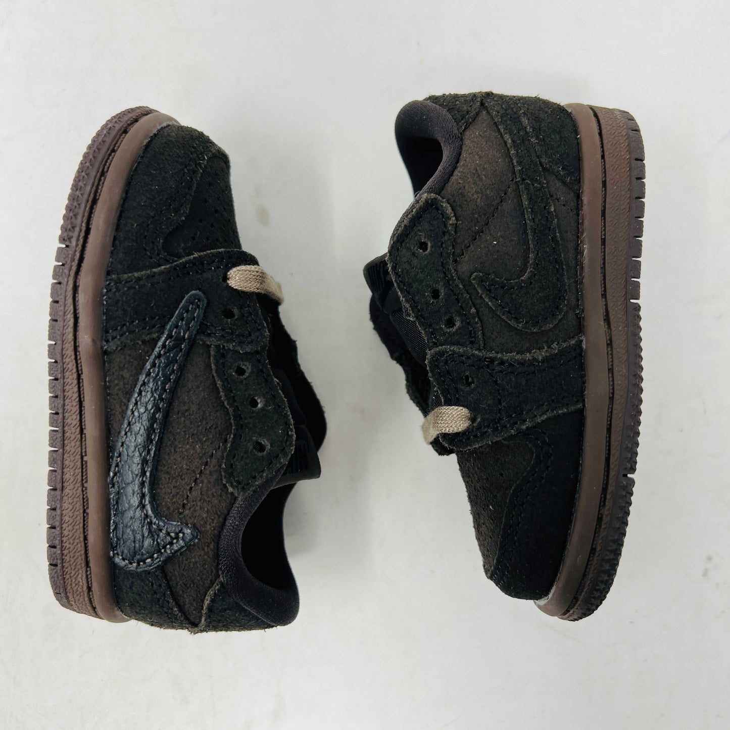 A Jordan 1 Retro Low OG SP Travis Scott Velvet Brown (TD) sneaker with a unique swoosh design sits on a white shoebox. It includes extra pink and black laces, is 100% authentic, brand new, and ready to elevate your style with its sleek look.