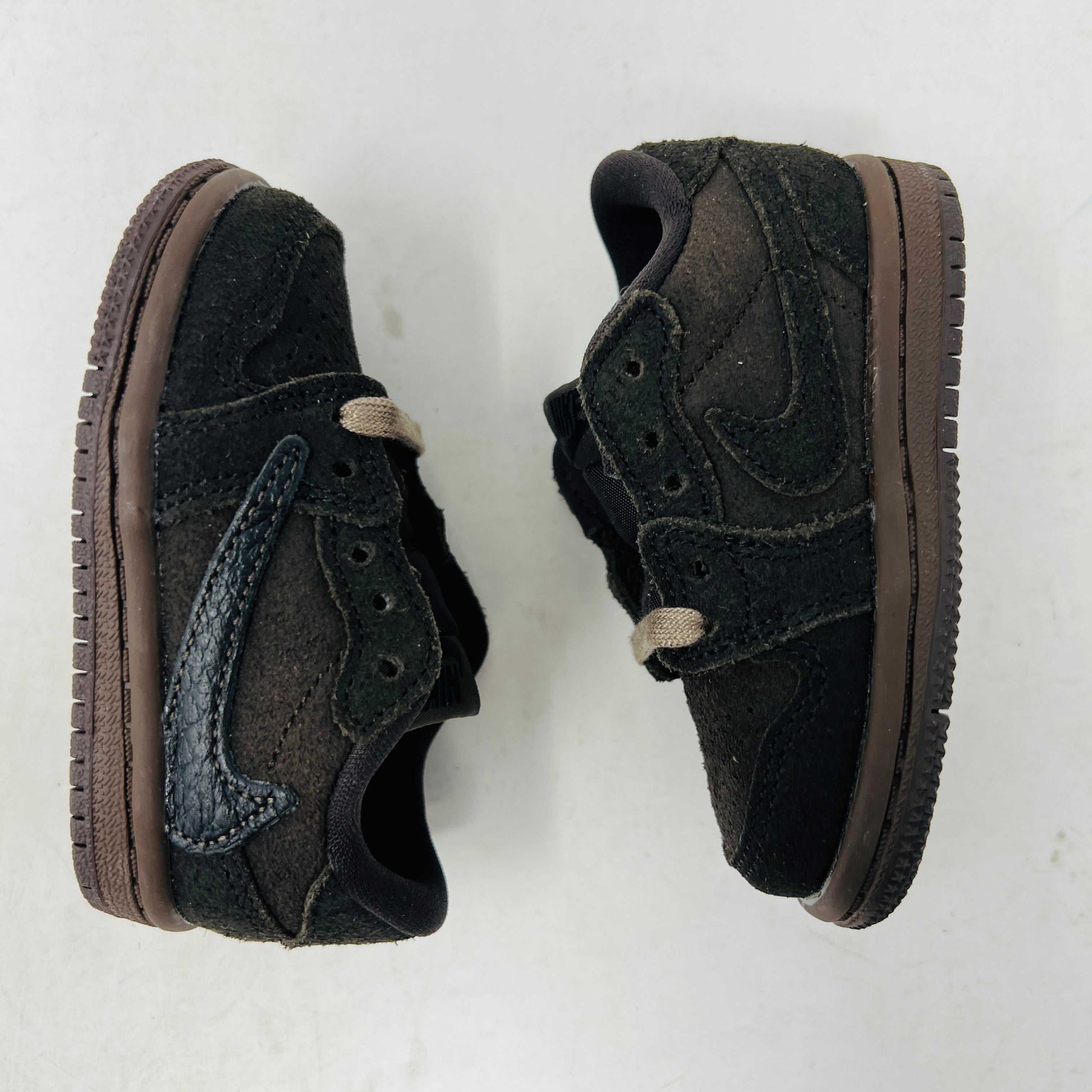 A Jordan 1 Retro Low OG SP Travis Scott Velvet Brown (TD) sneaker with a unique swoosh design sits on a white shoebox. It includes extra pink and black laces, is 100% authentic, brand new, and ready to elevate your style with its sleek look.