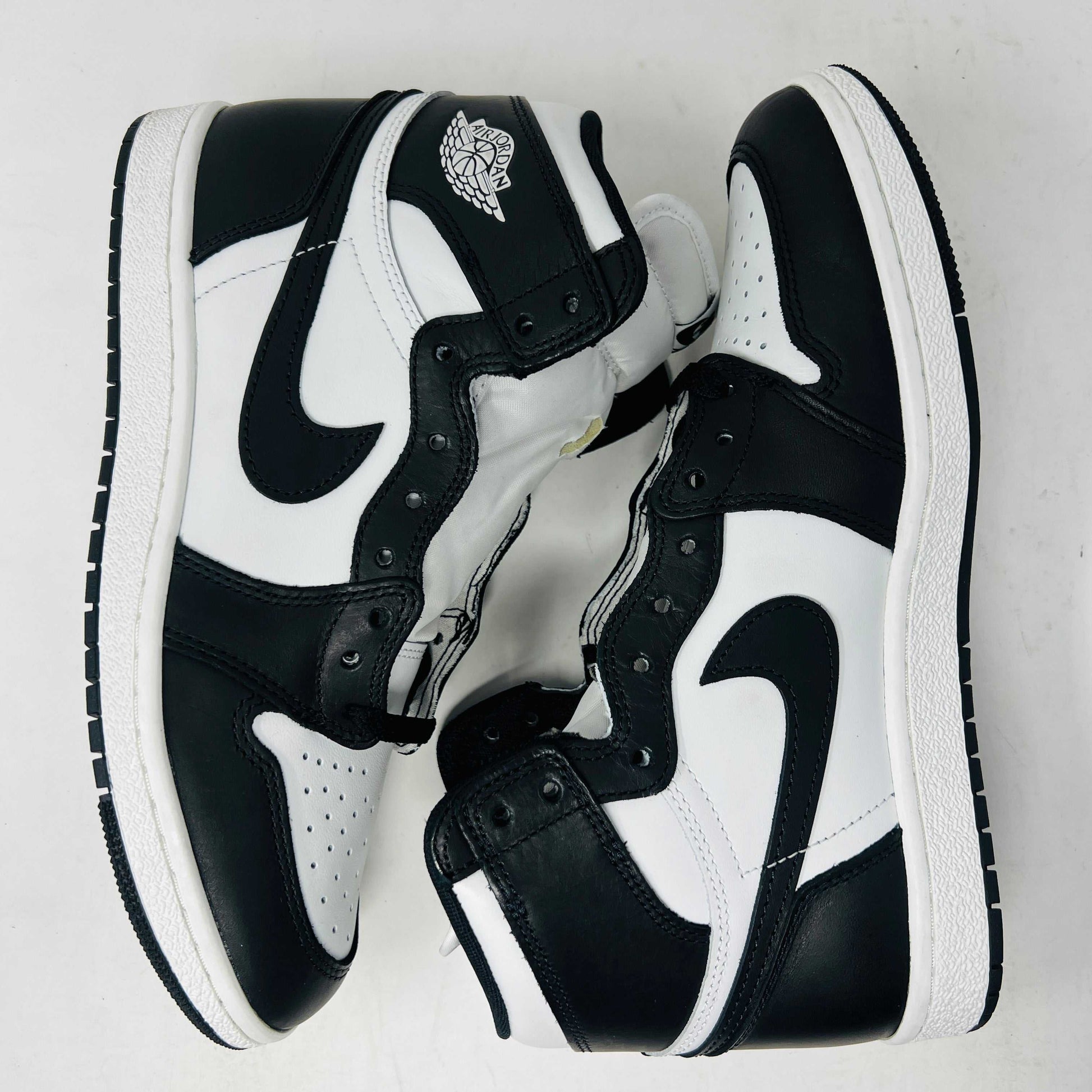 A Jordan 1 Retro High 85 Black White (2023) sneaker is showcased on a red Nike box. This black and white high-top features the Air Jordan logo and includes extra white laces.