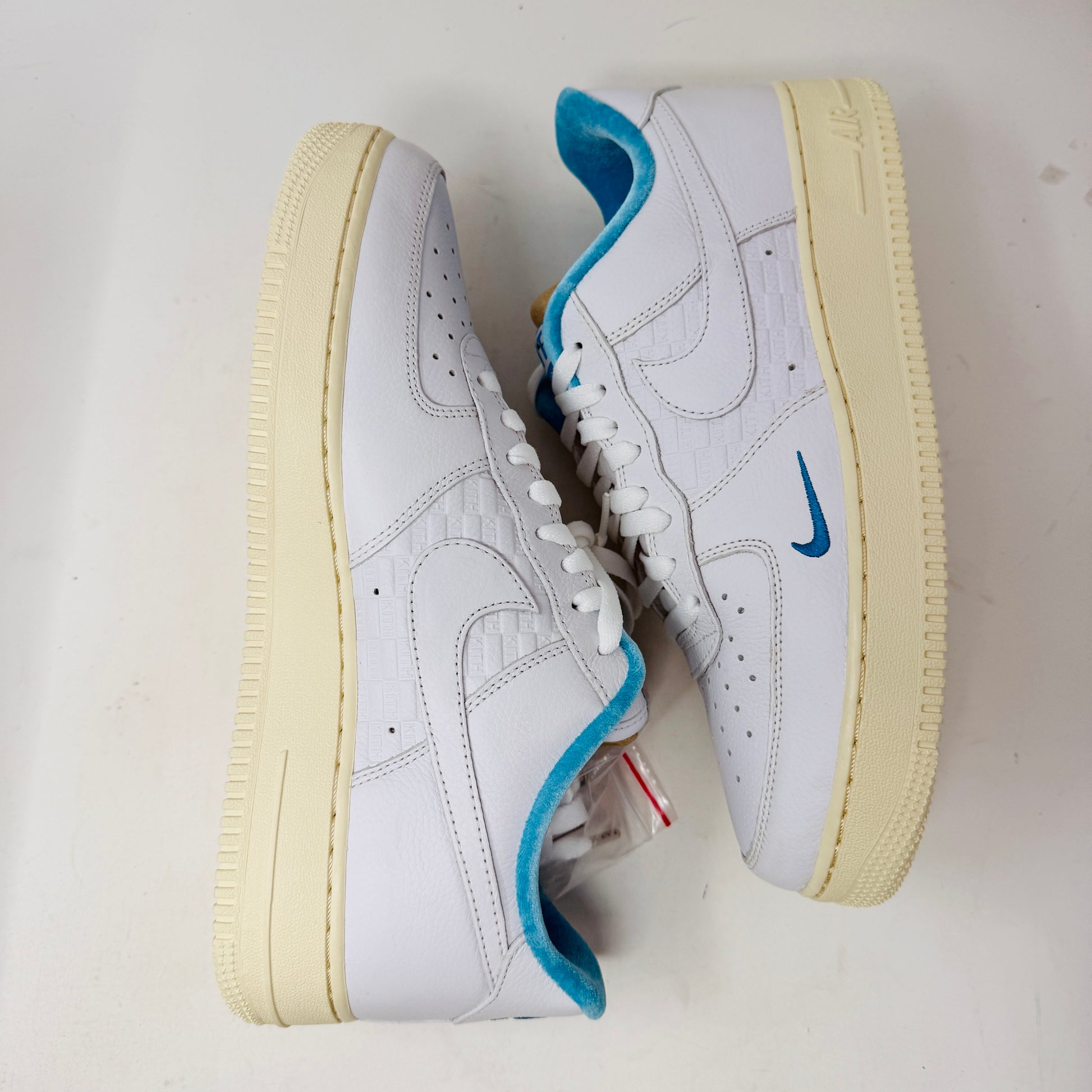 Introducing the Nike Air Force 1 Low Kith Hawaii sneaker: a fresh white design with white laces, light blue inner lining, teal swoosh, textured pattern, and cream-colored sole. Packaged in a gray shoebox, it features the word AIR embossed on the side.