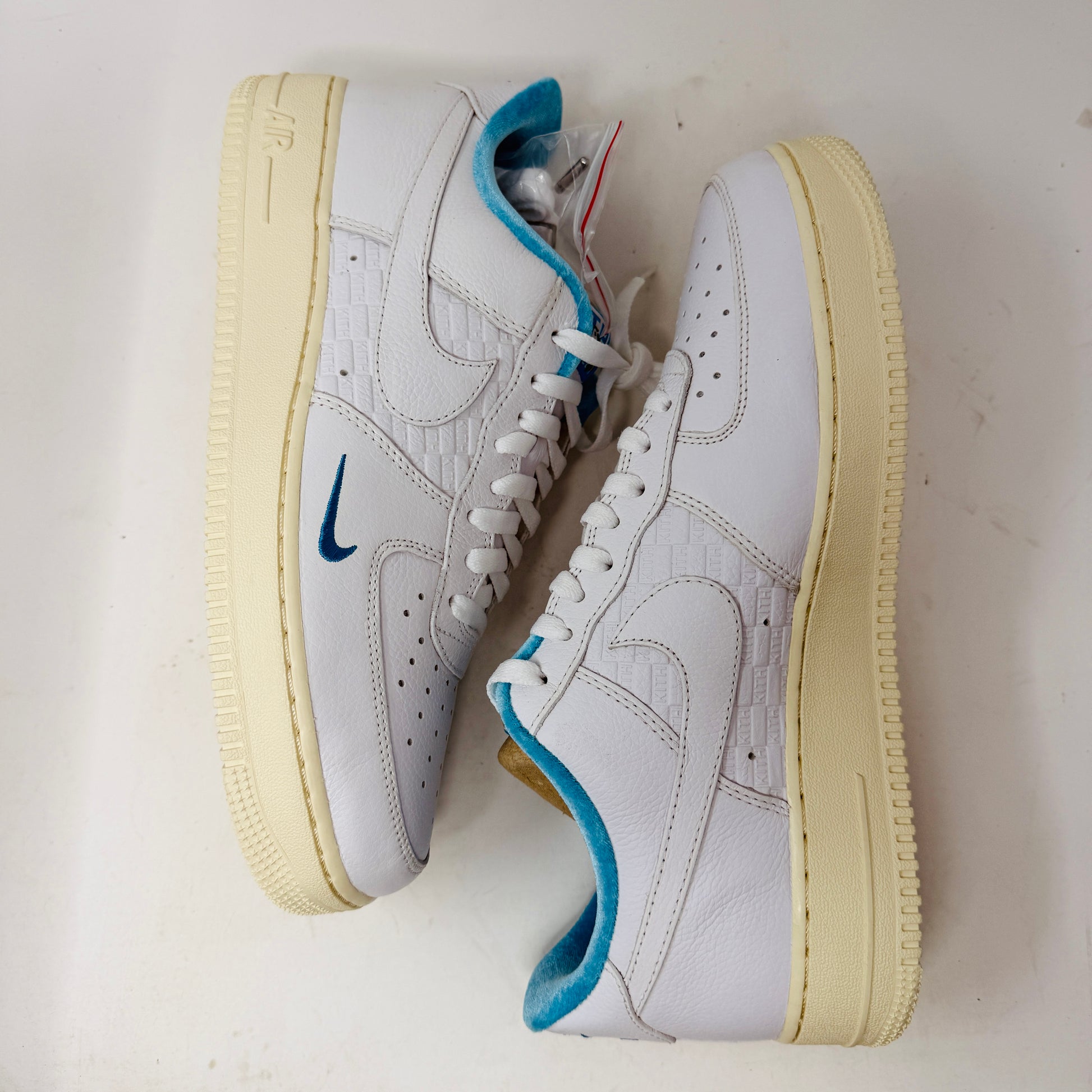 Introducing the Nike Air Force 1 Low Kith Hawaii sneaker: a fresh white design with white laces, light blue inner lining, teal swoosh, textured pattern, and cream-colored sole. Packaged in a gray shoebox, it features the word AIR embossed on the side.