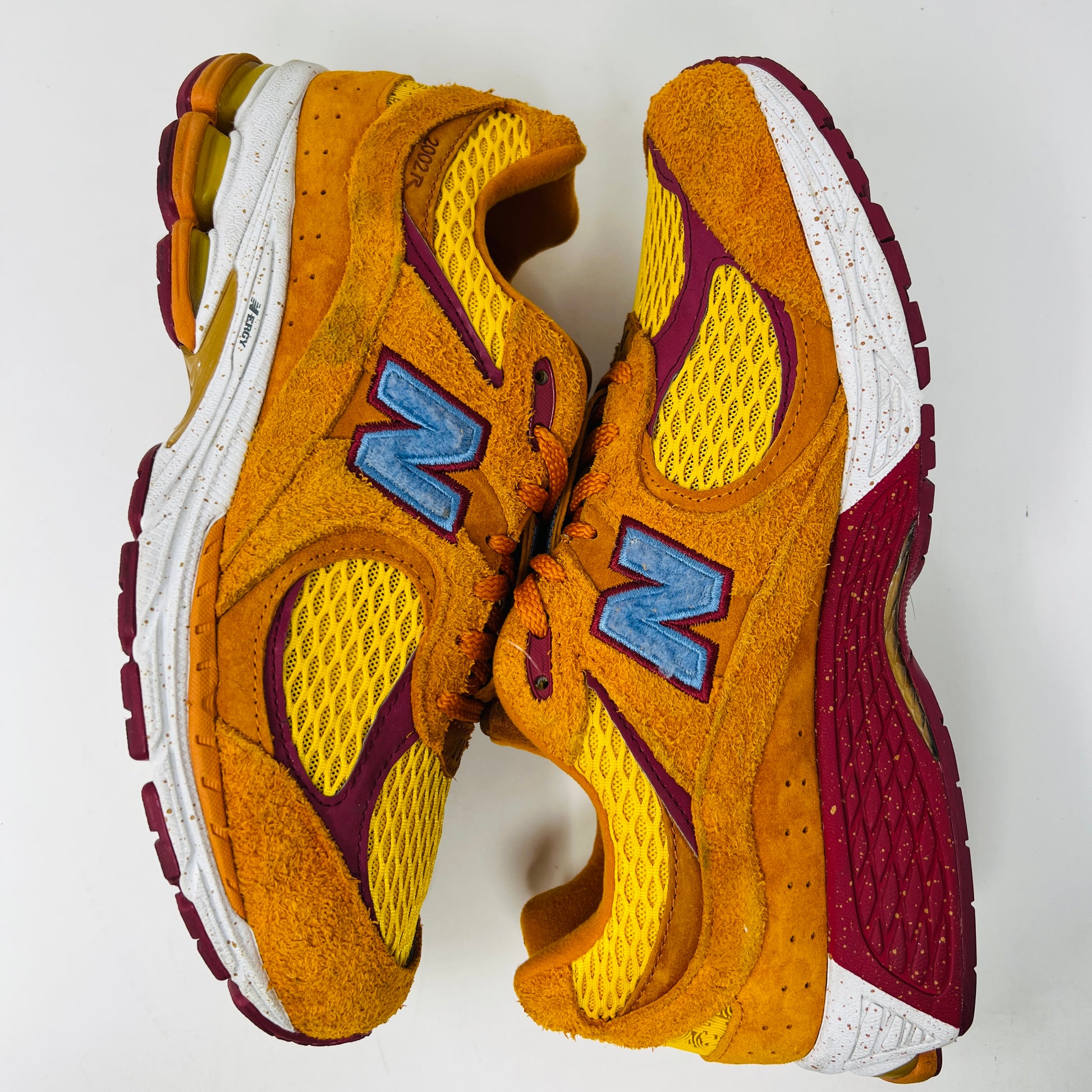 A New Balance 2002R Salehe Bembury Peace Be The Journey sneaker in vibrant orange and yellow with a blue N logo is displayed on a shoebox. It features textured design, visible sole cushioning, and extra laces. Tagged as model ML2002R1, size 10.5, priced at $330.