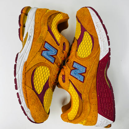 A New Balance 2002R Salehe Bembury Peace Be The Journey sneaker in vibrant orange and yellow with a blue N logo is displayed on a shoebox. It features textured design, visible sole cushioning, and extra laces. Tagged as model ML2002R1, size 10.5, priced at $330.