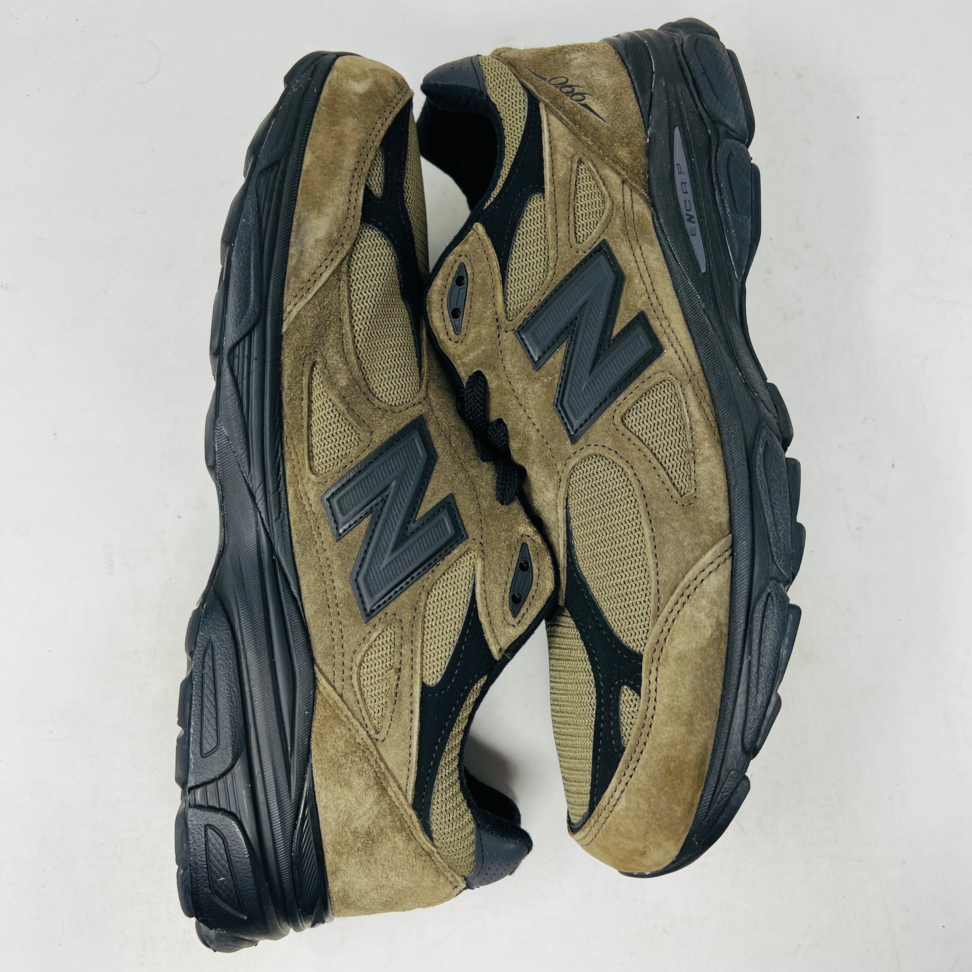 The New Balance 990v3 MiUSA JJJJound Brown Black athletic shoe, released in 2022, features tan and black mesh-suede uppers with an N logo on the side and 990 on the heel. It sits atop a black shoebox with the label M990JJ3 and shows light wear.