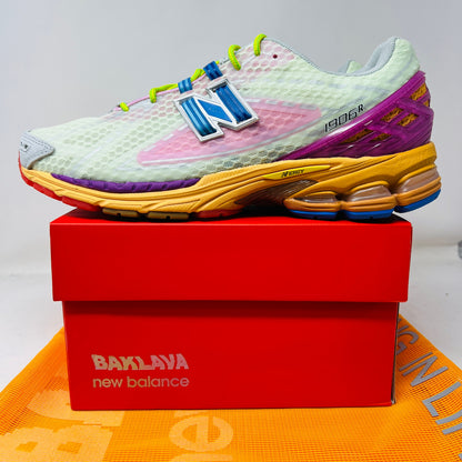 The New Balance 1906R Action Bronson Rosewater sneaker, boasting a light mesh upper and colorful sole with a bold blue N logo, rests on a pristine red Baylaya box. An orange surface partially peeks out under the box.