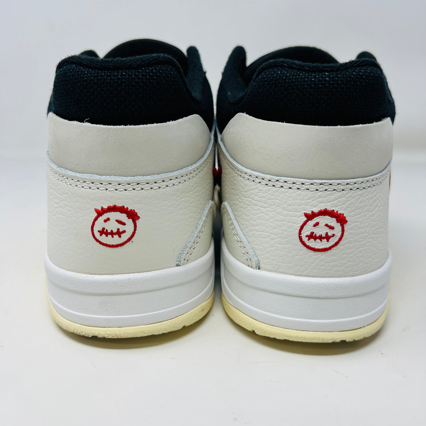 The Jordan Jumpman Jack TR Travis Scott University Red sneakers, black and white with red swooshes, rest on a brown shoe box. Three lace sets in red, cream, and black with white speckles are individually packaged in front. The box label displays sizes 9 and 10.5.