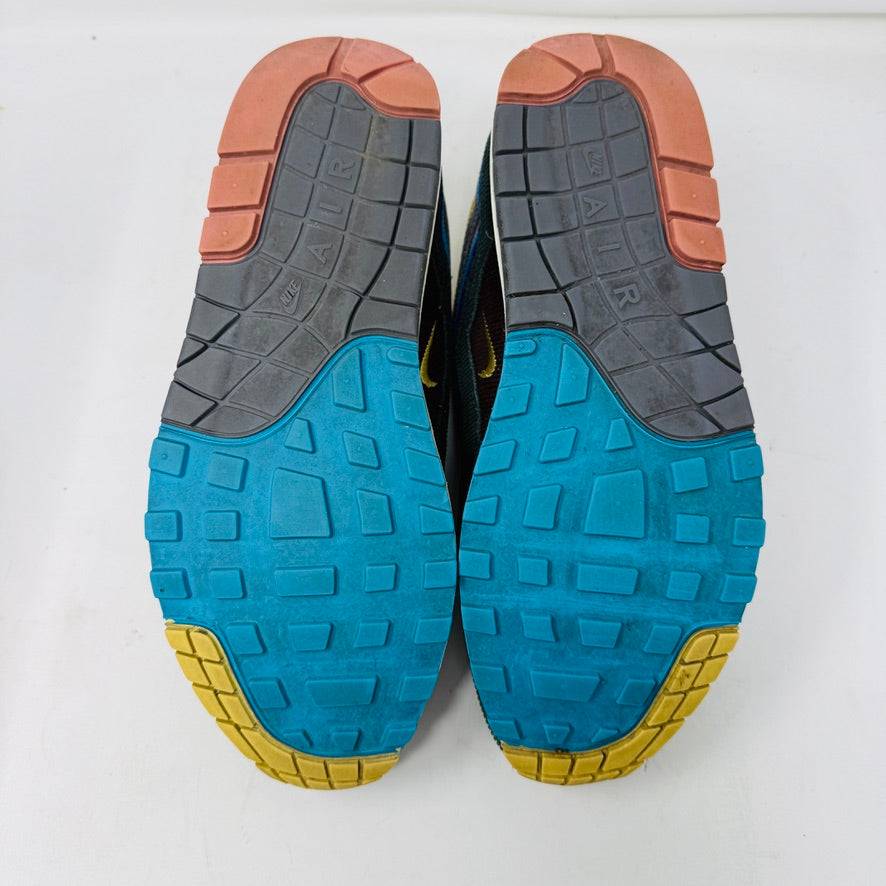 The Nike Air Max 1/97 Sean Wotherspoon sneaker, featuring a multicolored wave-like design, rests on a New Balance box and includes extra blue, white, and dark blue laces. It showcases an authentic air cushion in the sole.
