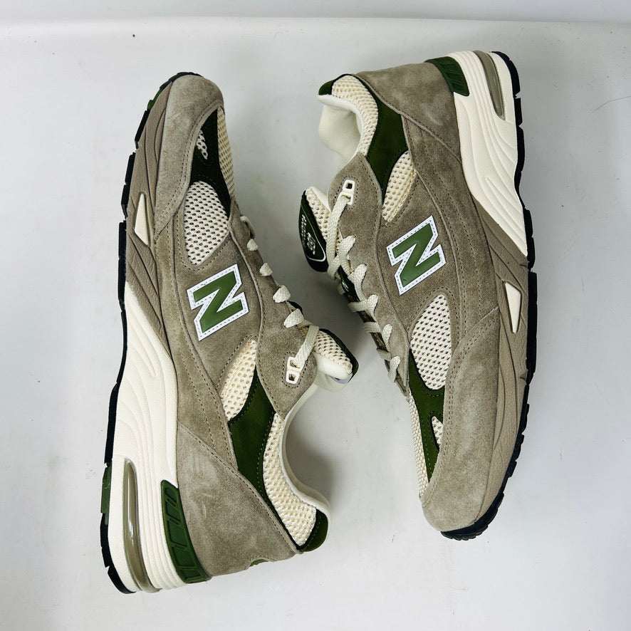 A pair of Holy Grounds New Balance 991 Aime Leon Dore MiUK Grey sneakers in gray, green, and beige are displayed on their shoebox. Comes with extra green and gray laces. The 2022 box details the size and model.