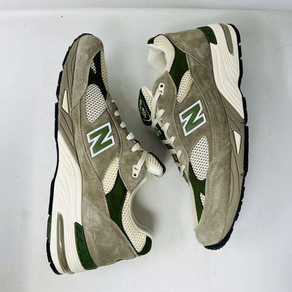 A pair of Holy Grounds New Balance 991 Aime Leon Dore MiUK Grey sneakers in gray, green, and beige are displayed on their shoebox. Comes with extra green and gray laces. The 2022 box details the size and model.