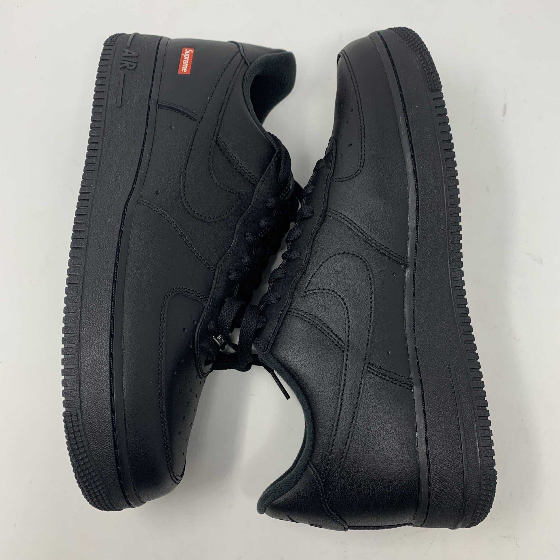 The Nike Supreme Air Force 1 Black features a perforated design on the toe box, black supreme laces with a shiny tag, and a prominent Nike logo, all set against a plain white background.