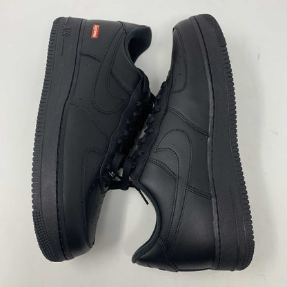 The Nike Supreme Air Force 1 Black features a perforated design on the toe box, black supreme laces with a shiny tag, and a prominent Nike logo, all set against a plain white background.