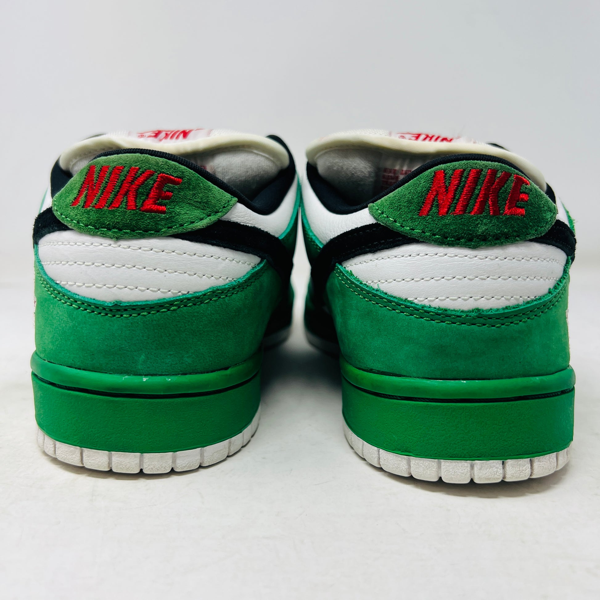 The Nike SB Dunk Low Heineken sneaker, featuring a green, white, and black design with red laces and a red star on the heel, sits on its box. A small package of green shoelaces is beside it. The box displays the size and Nike branding.