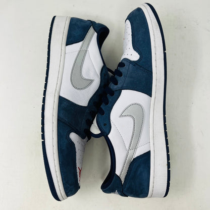 The Jordan 1 Low SB Midnight Navy sneakers, with white and navy panels and a side Nike swoosh, are displayed on a pristine shoebox. A spare set of white laces featuring the Nike SB logo in Metallic Silver is also included.