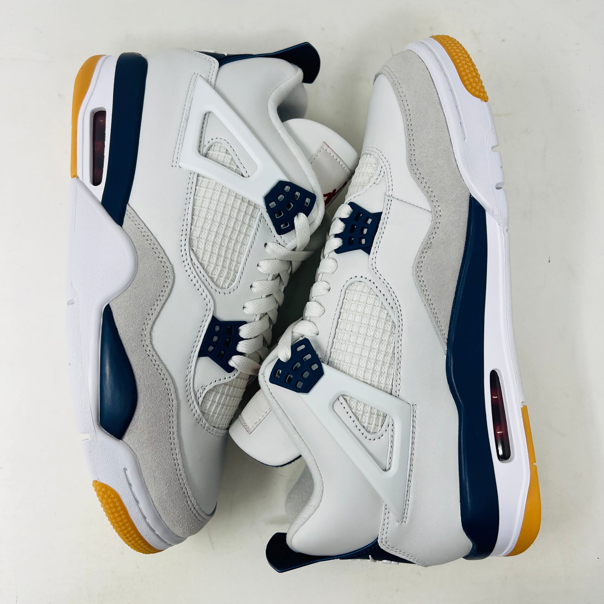 The Jordan 4 Retro SB Navy from Holy Ground Sneaker Shop, with white and navy mesh and orange details, sits on a pristine box showcasing the Nike SB logo. Its cushioned heel ensures its a perfect accessory addition.