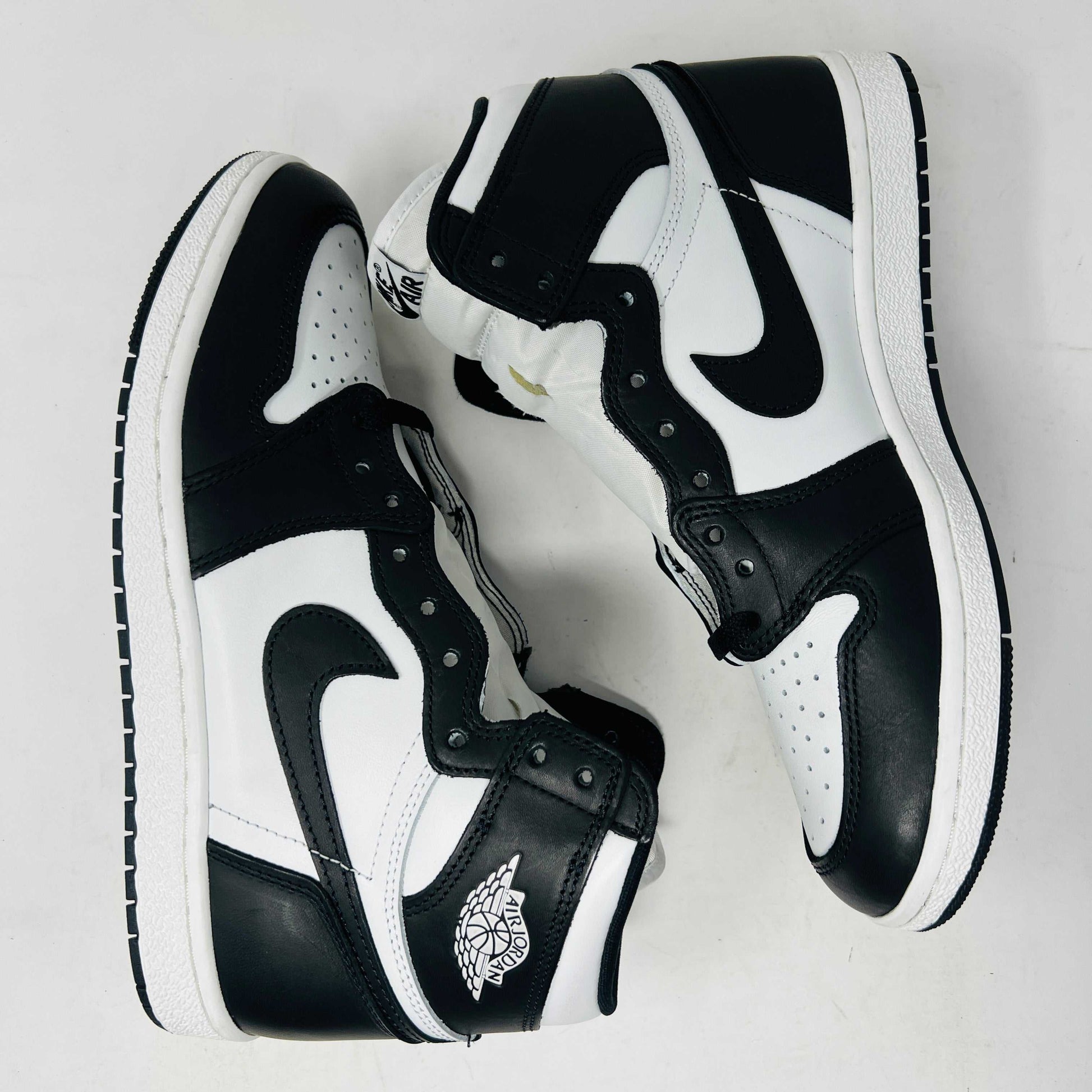 A Jordan 1 Retro High 85 Black White (2023) sneaker is showcased on a red Nike box. This black and white high-top features the Air Jordan logo and includes extra white laces.
