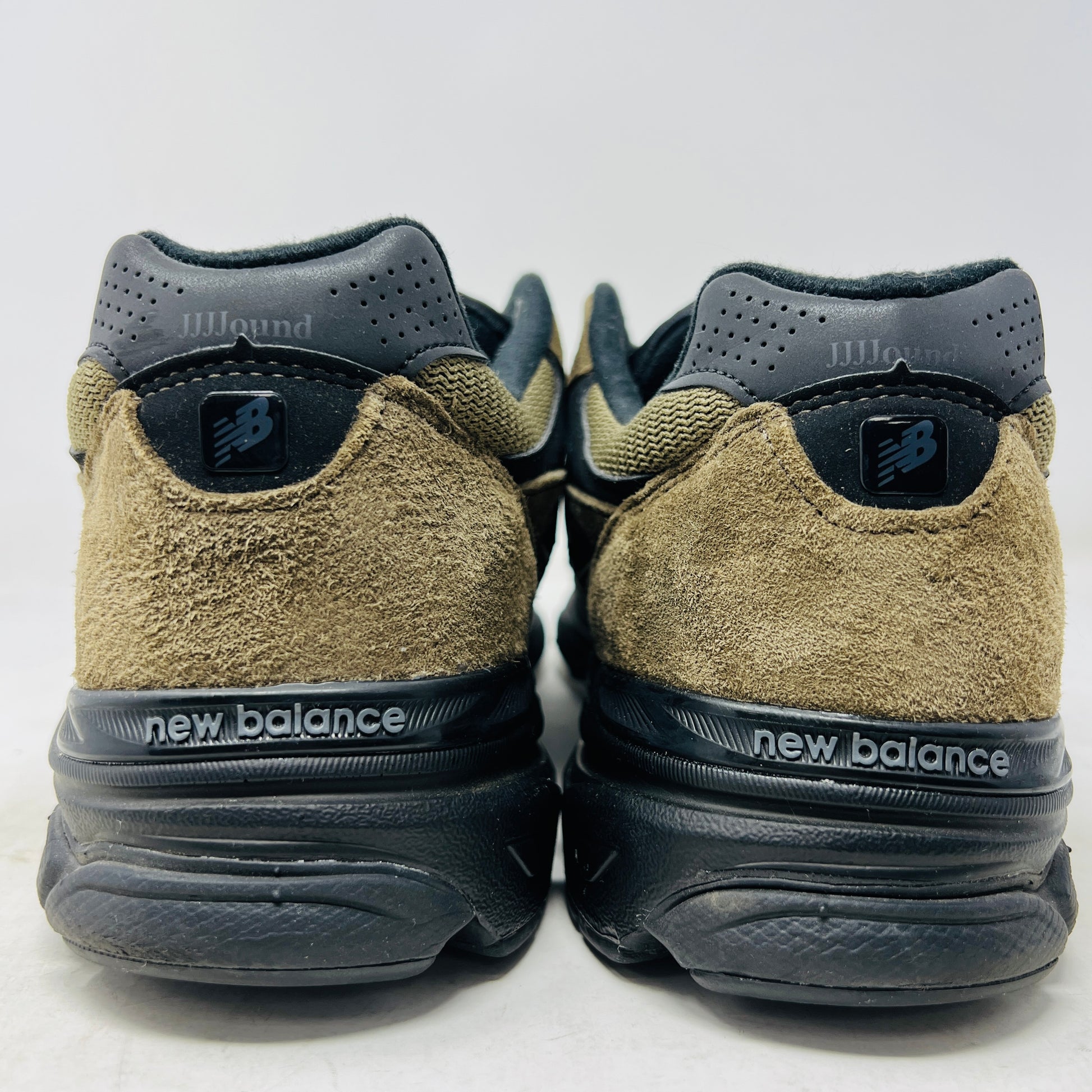 The New Balance 990v3 MiUSA JJJJound Brown Black athletic shoe, released in 2022, features tan and black mesh-suede uppers with an N logo on the side and 990 on the heel. It sits atop a black shoebox with the label M990JJ3 and shows light wear.