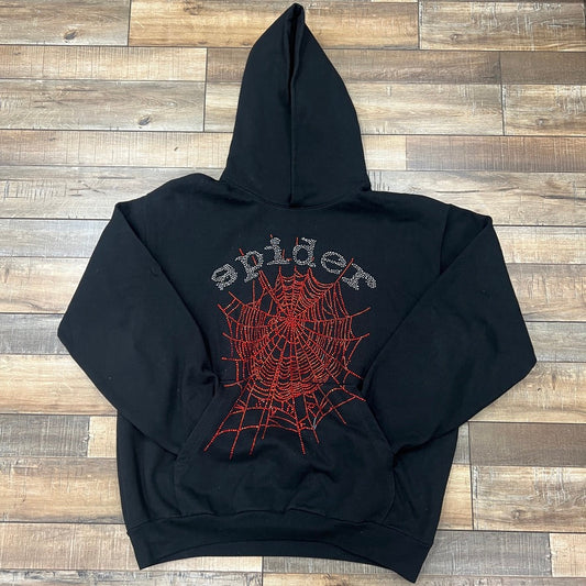 Sp5der Rhinestone OG Web Hoodie Black with red web design on wooden floor.