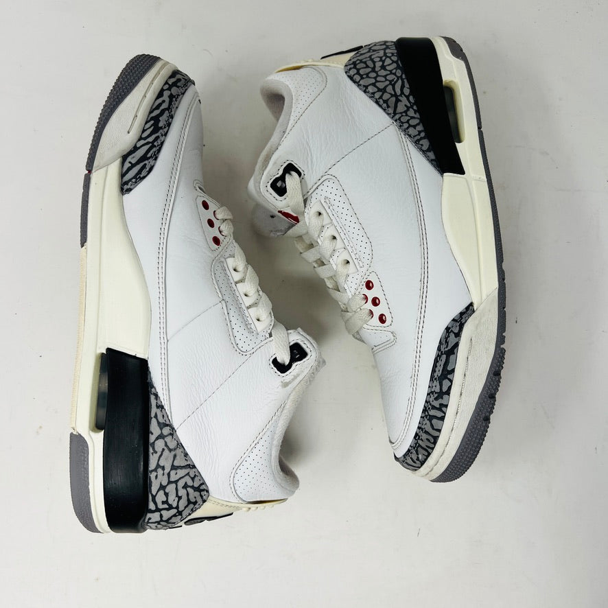 The Jordan 3 Retro White Cement Reimagined sneakers by Jordan feature a clean white upper with red accents, gray and black patterned trim on the toe and heel, white laces, and a red logo on the tongue, displayed upright on a pristine white background—perfect for everyday wear.