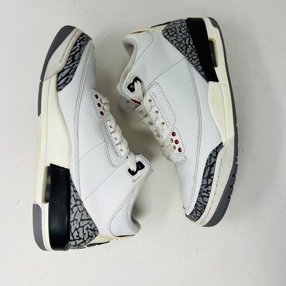 The Jordan 3 Retro White Cement Reimagined sneakers by Jordan feature a clean white upper with red accents, gray and black patterned trim on the toe and heel, white laces, and a red logo on the tongue, displayed upright on a pristine white background—perfect for everyday wear.