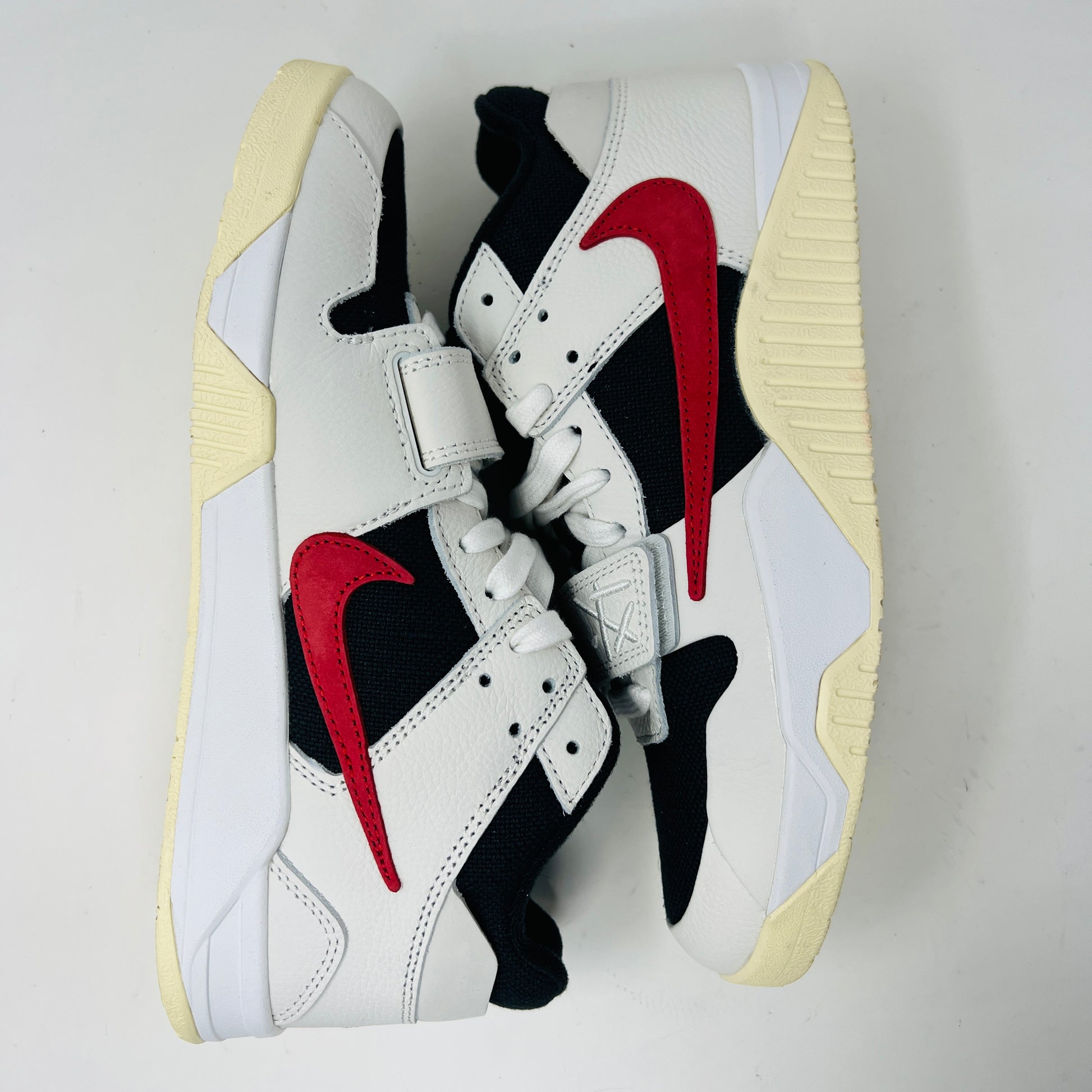 The Jordan Jumpman Jack TR Travis Scott University Red sneakers, black and white with red swooshes, rest on a brown shoe box. Three lace sets in red, cream, and black with white speckles are individually packaged in front. The box label displays sizes 9 and 10.5.