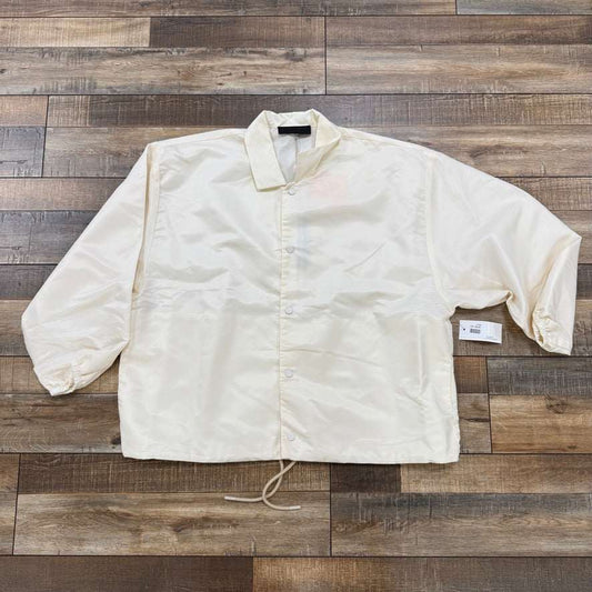 God Essentials Coaches Jacket Cloud Dancer, brand new condition, cream white color displayed flat.