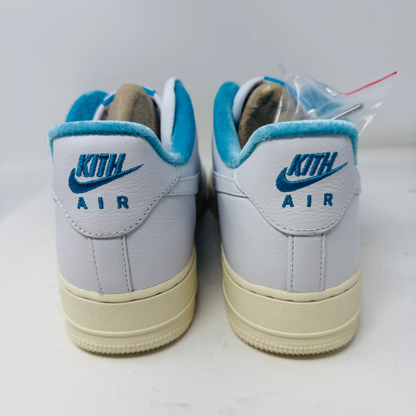 Introducing the Nike Air Force 1 Low Kith Hawaii sneaker: a fresh white design with white laces, light blue inner lining, teal swoosh, textured pattern, and cream-colored sole. Packaged in a gray shoebox, it features the word AIR embossed on the side.
