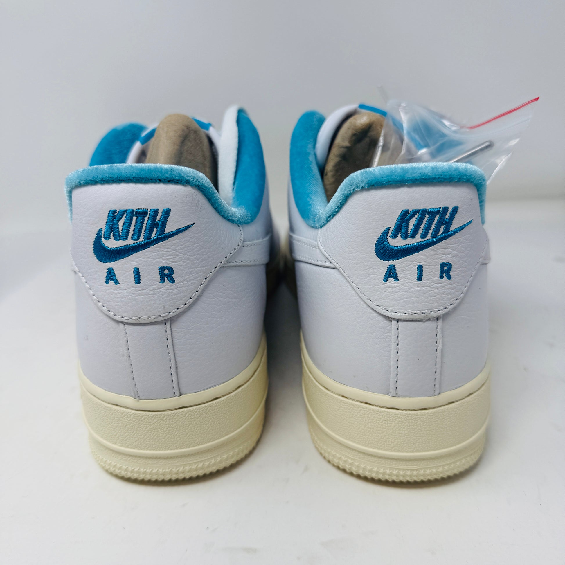 Introducing the Nike Air Force 1 Low Kith Hawaii sneaker: a fresh white design with white laces, light blue inner lining, teal swoosh, textured pattern, and cream-colored sole. Packaged in a gray shoebox, it features the word AIR embossed on the side.