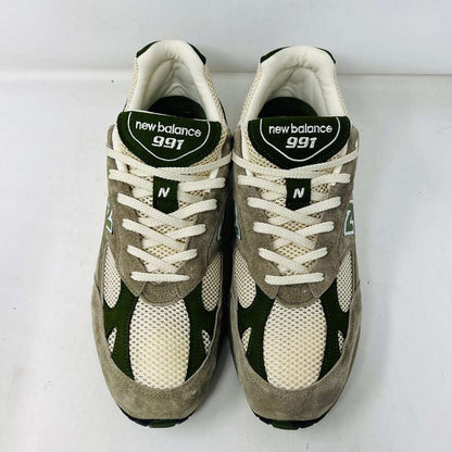 A pair of Holy Grounds New Balance 991 Aime Leon Dore MiUK Grey sneakers in gray, green, and beige are displayed on their shoebox. Comes with extra green and gray laces. The 2022 box details the size and model.