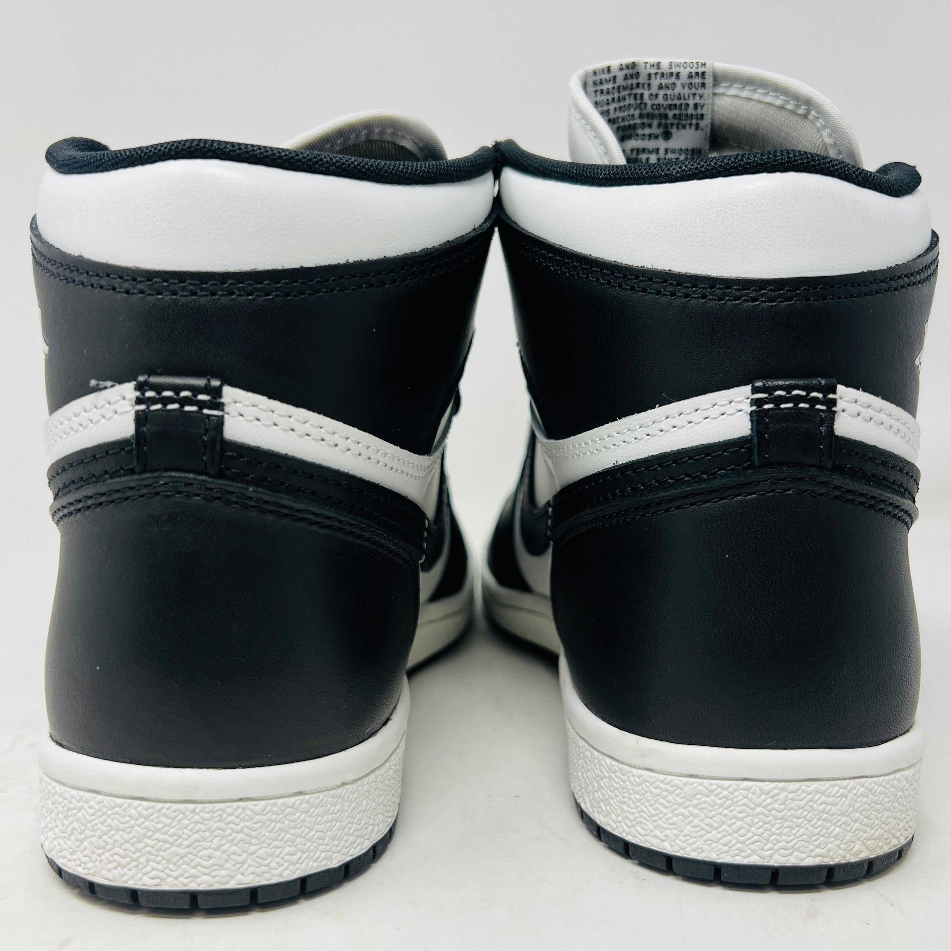 A Jordan 1 Retro High 85 Black White (2023) sneaker is showcased on a red Nike box. This black and white high-top features the Air Jordan logo and includes extra white laces.