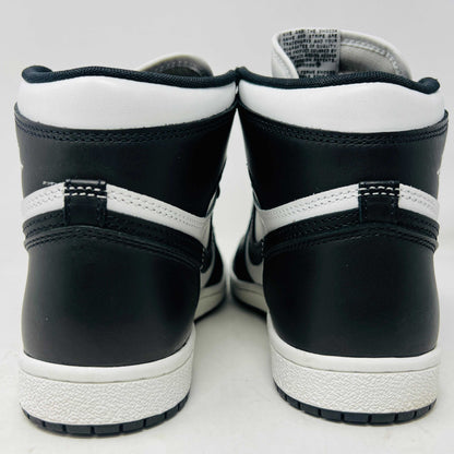 A Jordan 1 Retro High 85 Black White (2023) sneaker is showcased on a red Nike box. This black and white high-top features the Air Jordan logo and includes extra white laces.