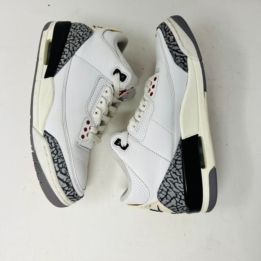 The Jordan 3 Retro White Cement Reimagined sneakers by Jordan feature a clean white upper with red accents, gray and black patterned trim on the toe and heel, white laces, and a red logo on the tongue, displayed upright on a pristine white background—perfect for everyday wear.