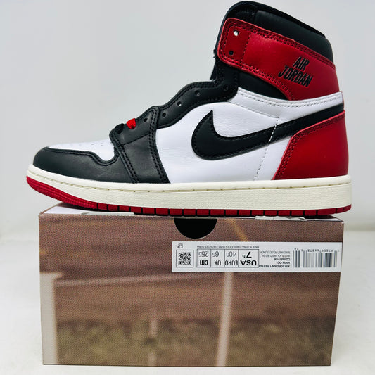 The Jordan 1 Retro High OG Black Toe Reimagined sits atop its box, featuring a black, white, and red design with a Nike swoosh and Air Jordan on the side. Sold by Holy Ground Sneaker Shop, it includes extra laces and a box lid with detailed product information and bold side designs.