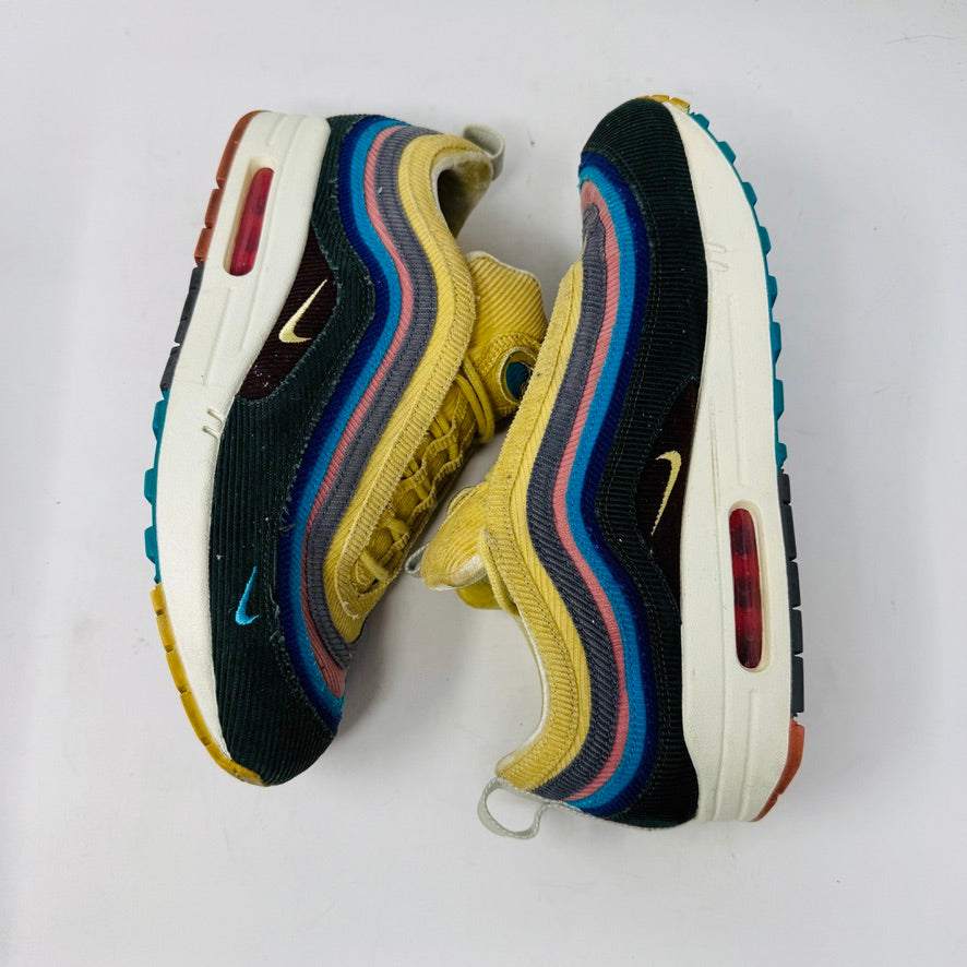 The Nike Air Max 1/97 Sean Wotherspoon sneaker, featuring a multicolored wave-like design, rests on a New Balance box and includes extra blue, white, and dark blue laces. It showcases an authentic air cushion in the sole.
