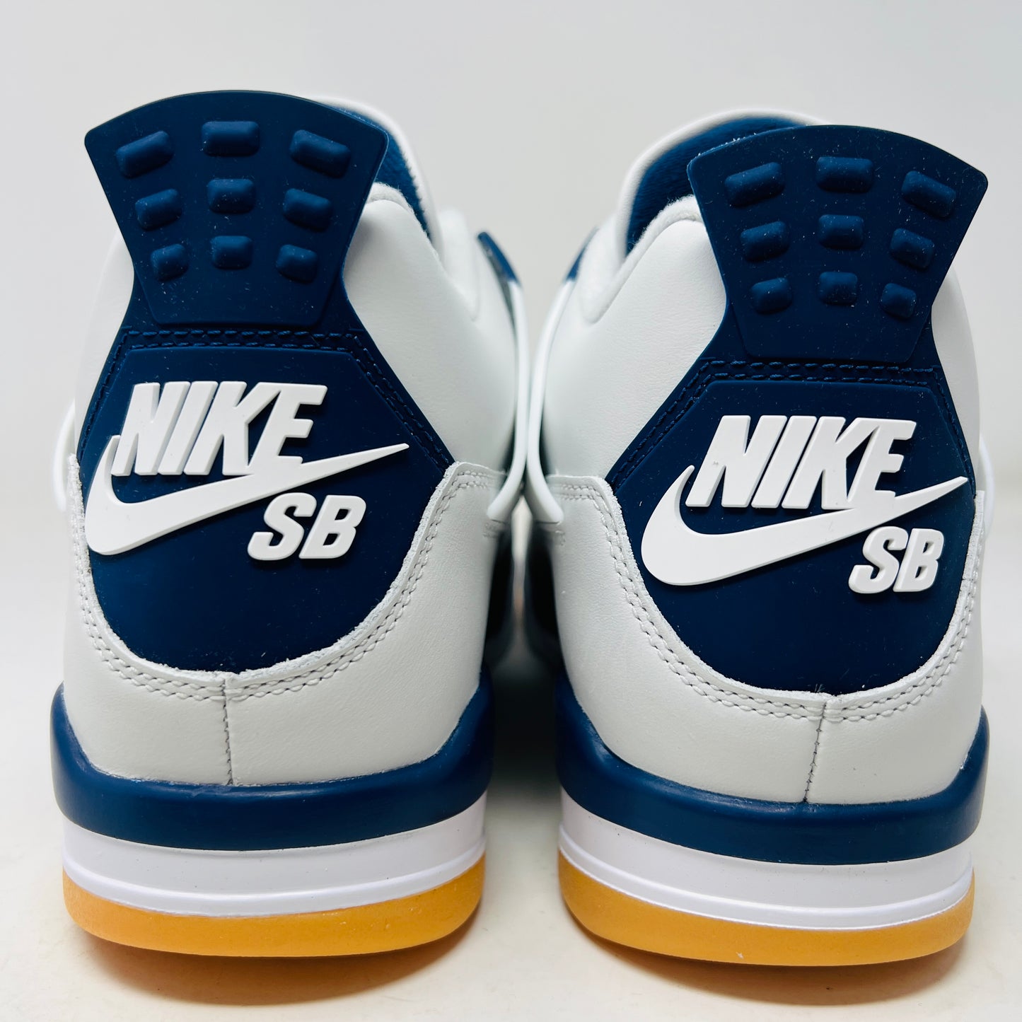 The Jordan 4 Retro SB Navy from Holy Ground Sneaker Shop, with white and navy mesh and orange details, sits on a pristine box showcasing the Nike SB logo. Its cushioned heel ensures its a perfect accessory addition.