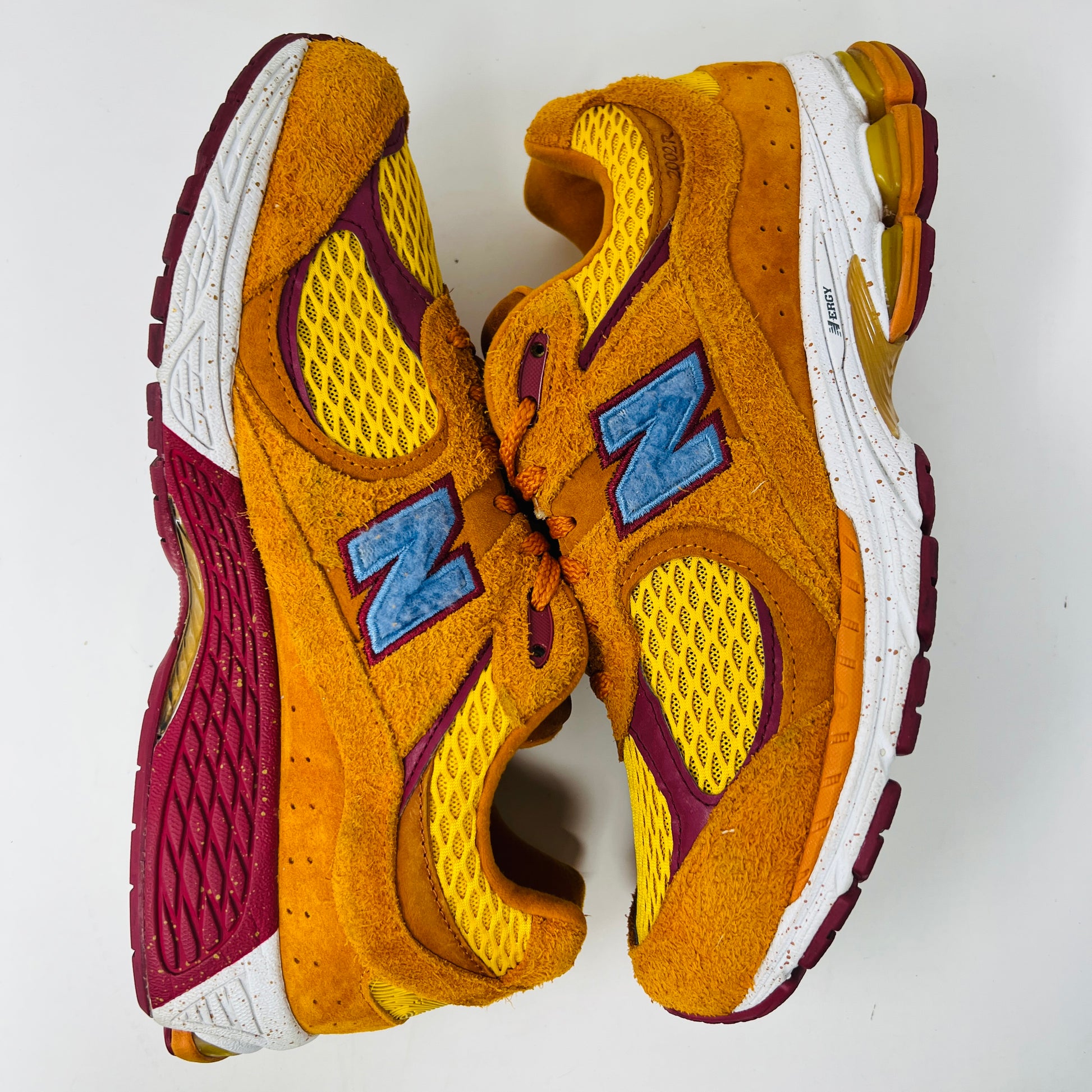 A New Balance 2002R Salehe Bembury Peace Be The Journey sneaker in vibrant orange and yellow with a blue N logo is displayed on a shoebox. It features textured design, visible sole cushioning, and extra laces. Tagged as model ML2002R1, size 10.5, priced at $330.