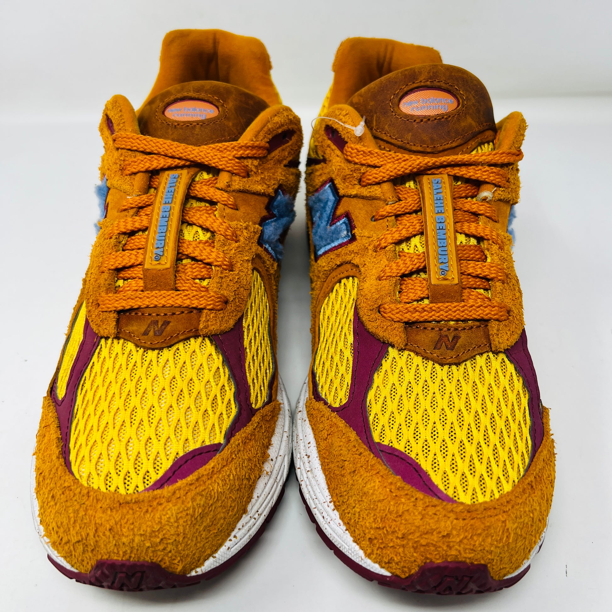 A New Balance 2002R Salehe Bembury Peace Be The Journey sneaker in vibrant orange and yellow with a blue N logo is displayed on a shoebox. It features textured design, visible sole cushioning, and extra laces. Tagged as model ML2002R1, size 10.5, priced at $330.