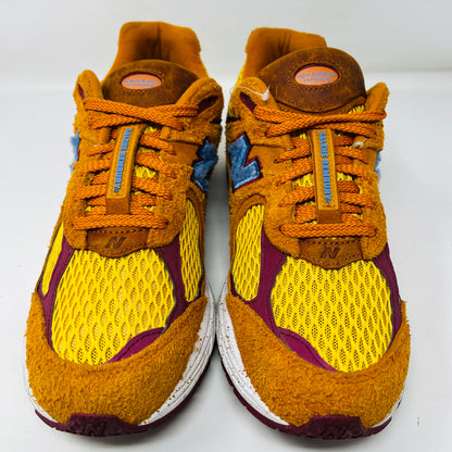 A New Balance 2002R Salehe Bembury Peace Be The Journey sneaker in vibrant orange and yellow with a blue N logo is displayed on a shoebox. It features textured design, visible sole cushioning, and extra laces. Tagged as model ML2002R1, size 10.5, priced at $330.