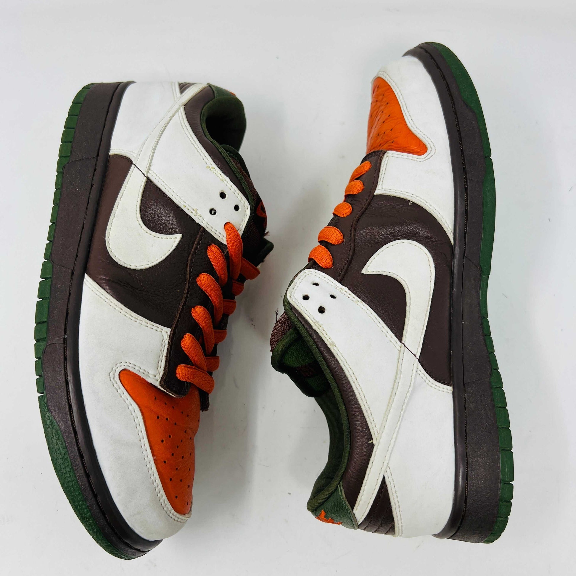 The Nike SB Dunk Low Oompa Loompa sneaker, in a brown, white, and orange color scheme with clean uppers, is displayed on its size 9.5 box. In the foreground is a packet of white laces with a Nike logo—guaranteed 100% authentic.