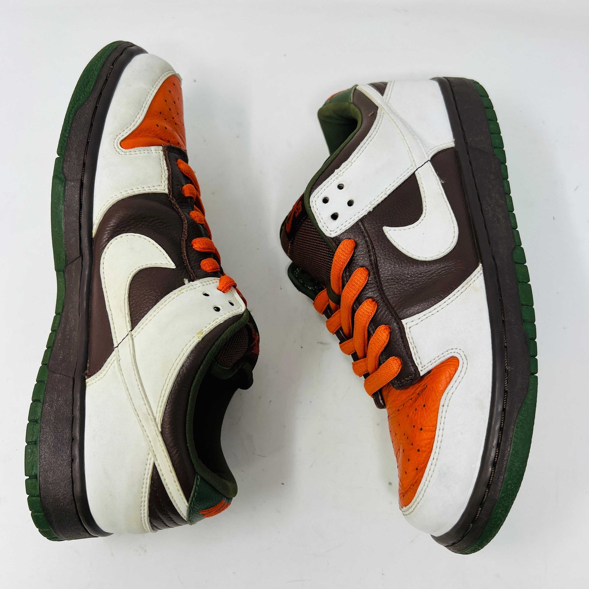 The Nike SB Dunk Low Oompa Loompa sneaker, in a brown, white, and orange color scheme with clean uppers, is displayed on its size 9.5 box. In the foreground is a packet of white laces with a Nike logo—guaranteed 100% authentic.