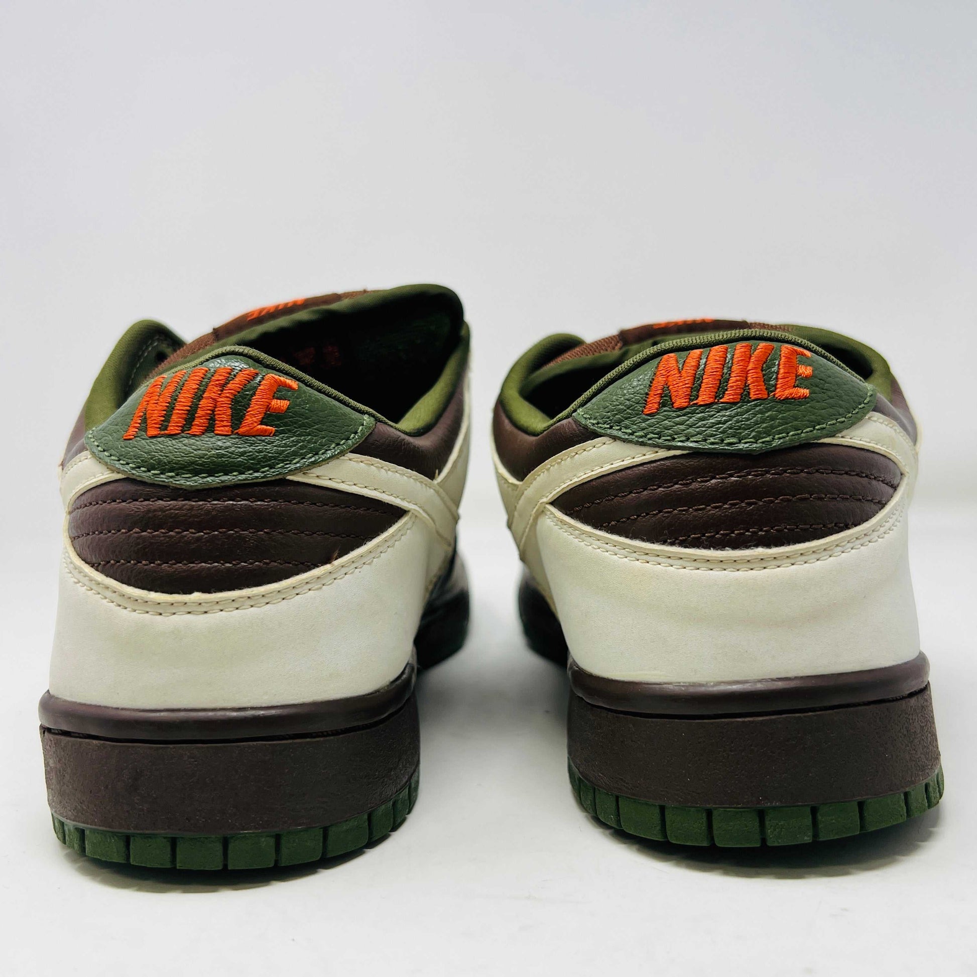 The Nike SB Dunk Low Oompa Loompa sneaker, in a brown, white, and orange color scheme with clean uppers, is displayed on its size 9.5 box. In the foreground is a packet of white laces with a Nike logo—guaranteed 100% authentic.