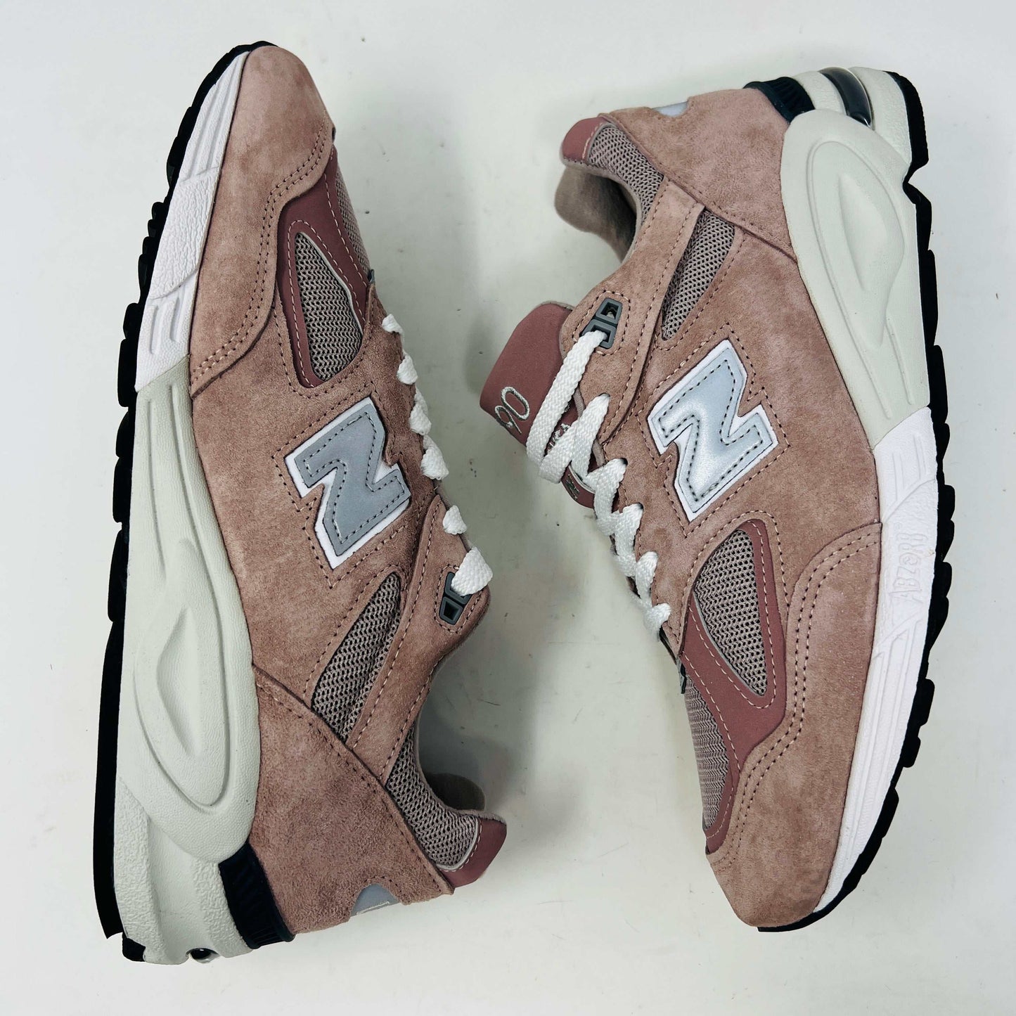 The New Balance 990v2 Kithstrike Rose sneaker from Holy Ground, in muted pink and gray, sits on its box labeled size 9.5 US, 9 UK, 43 EUR. Matching pink laces beside the box complete the authentic and stylish look with its clean uppers.
