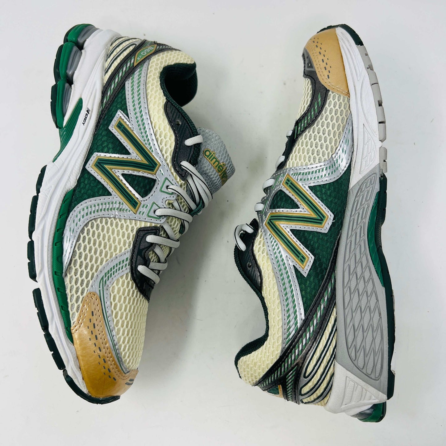 The New Balance 860v2 Aime Leon Dore Green sneaker, with mesh and leather uppers, features green and beige accents. Displayed on its box, it comes with cream and yellow laces for an authentic look.