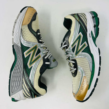 The New Balance 860v2 Aime Leon Dore Green sneaker, with mesh and leather uppers, features green and beige accents. Displayed on its box, it comes with cream and yellow laces for an authentic look.
