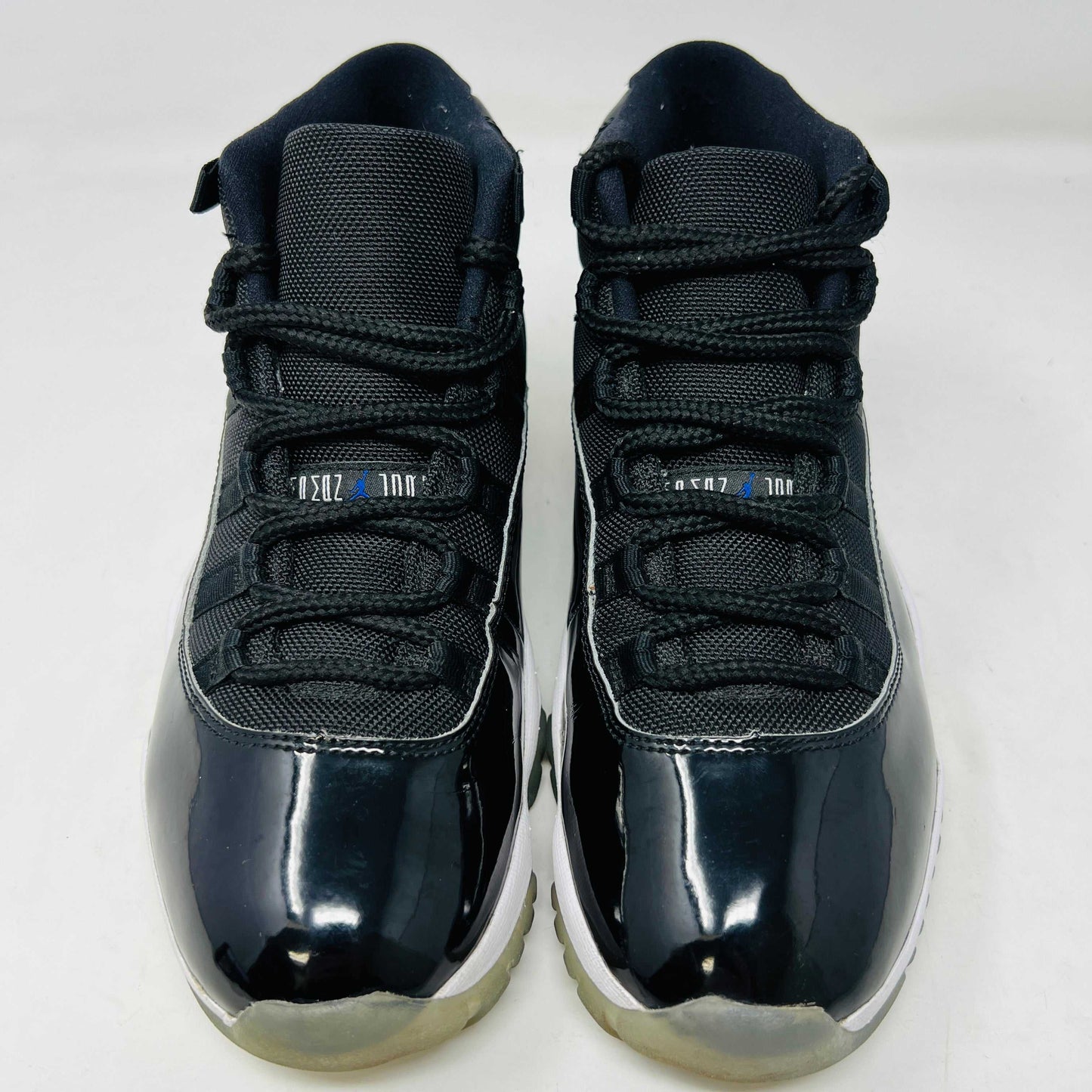 A Holy Ground Jordan 11 Retro Space Jam (2016) sneaker, featuring a glossy black patent leather upper with a blue Jumpman logo, sits on its original box. It has a white midsole and translucent outsole and is guaranteed 100% authentic with detailed sizing information on the box.