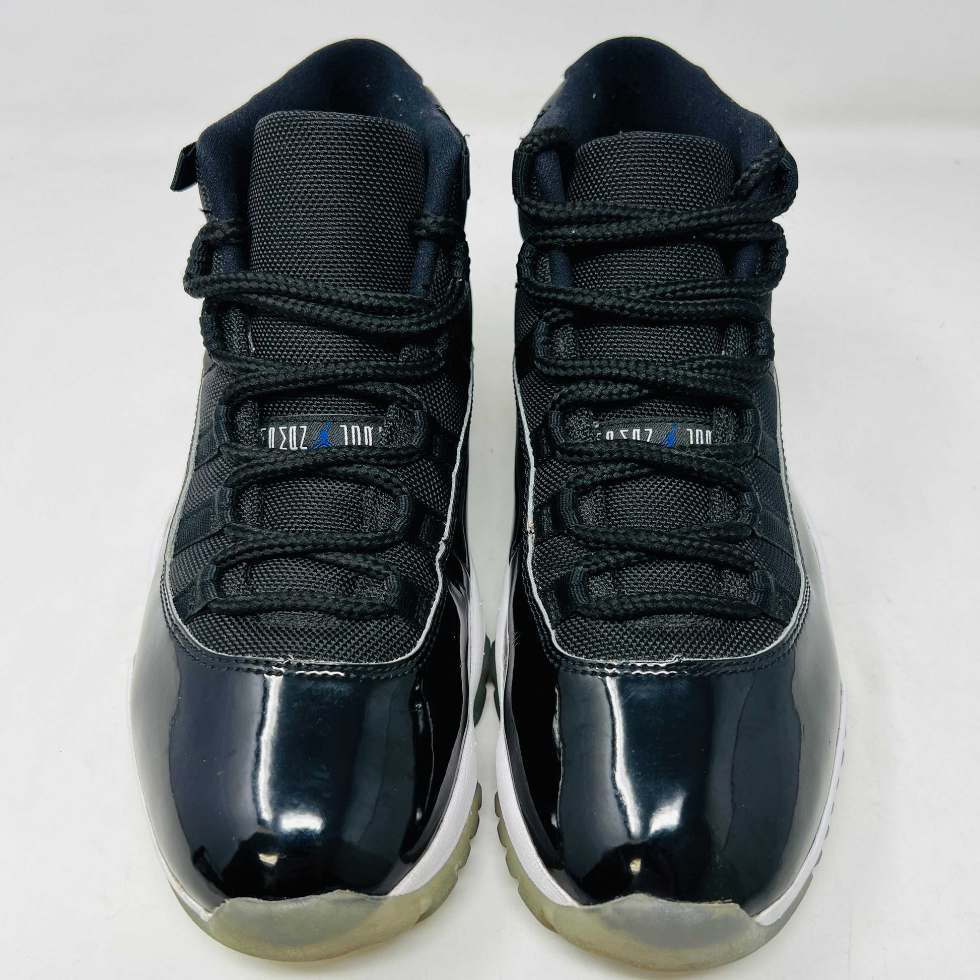 A Holy Ground Jordan 11 Retro Space Jam (2016) sneaker, featuring a glossy black patent leather upper with a blue Jumpman logo, sits on its original box. It has a white midsole and translucent outsole and is guaranteed 100% authentic with detailed sizing information on the box.