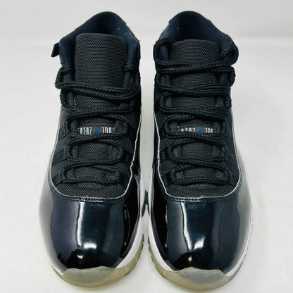 A Holy Ground Jordan 11 Retro Space Jam (2016) sneaker, featuring a glossy black patent leather upper with a blue Jumpman logo, sits on its original box. It has a white midsole and translucent outsole and is guaranteed 100% authentic with detailed sizing information on the box.