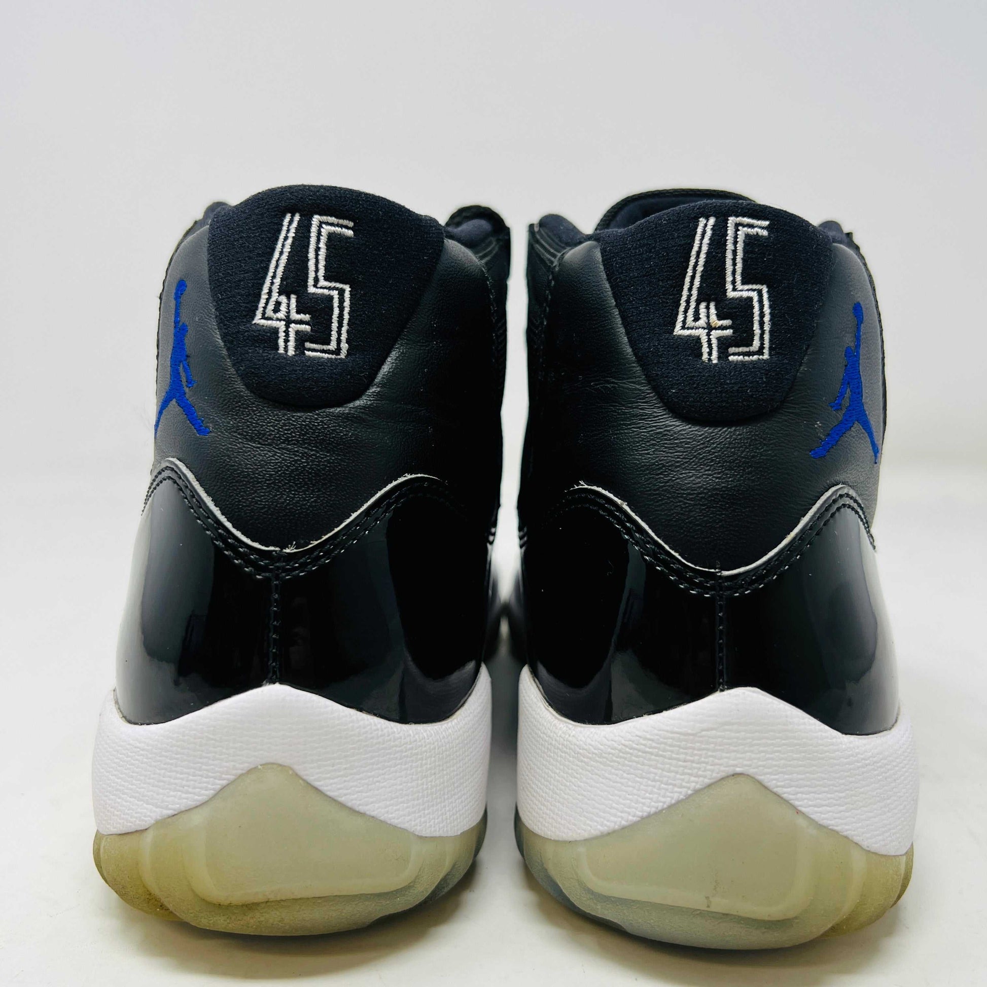 A Holy Ground Jordan 11 Retro Space Jam (2016) sneaker, featuring a glossy black patent leather upper with a blue Jumpman logo, sits on its original box. It has a white midsole and translucent outsole and is guaranteed 100% authentic with detailed sizing information on the box.