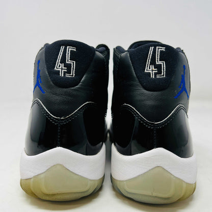 A Holy Ground Jordan 11 Retro Space Jam (2016) sneaker, featuring a glossy black patent leather upper with a blue Jumpman logo, sits on its original box. It has a white midsole and translucent outsole and is guaranteed 100% authentic with detailed sizing information on the box.