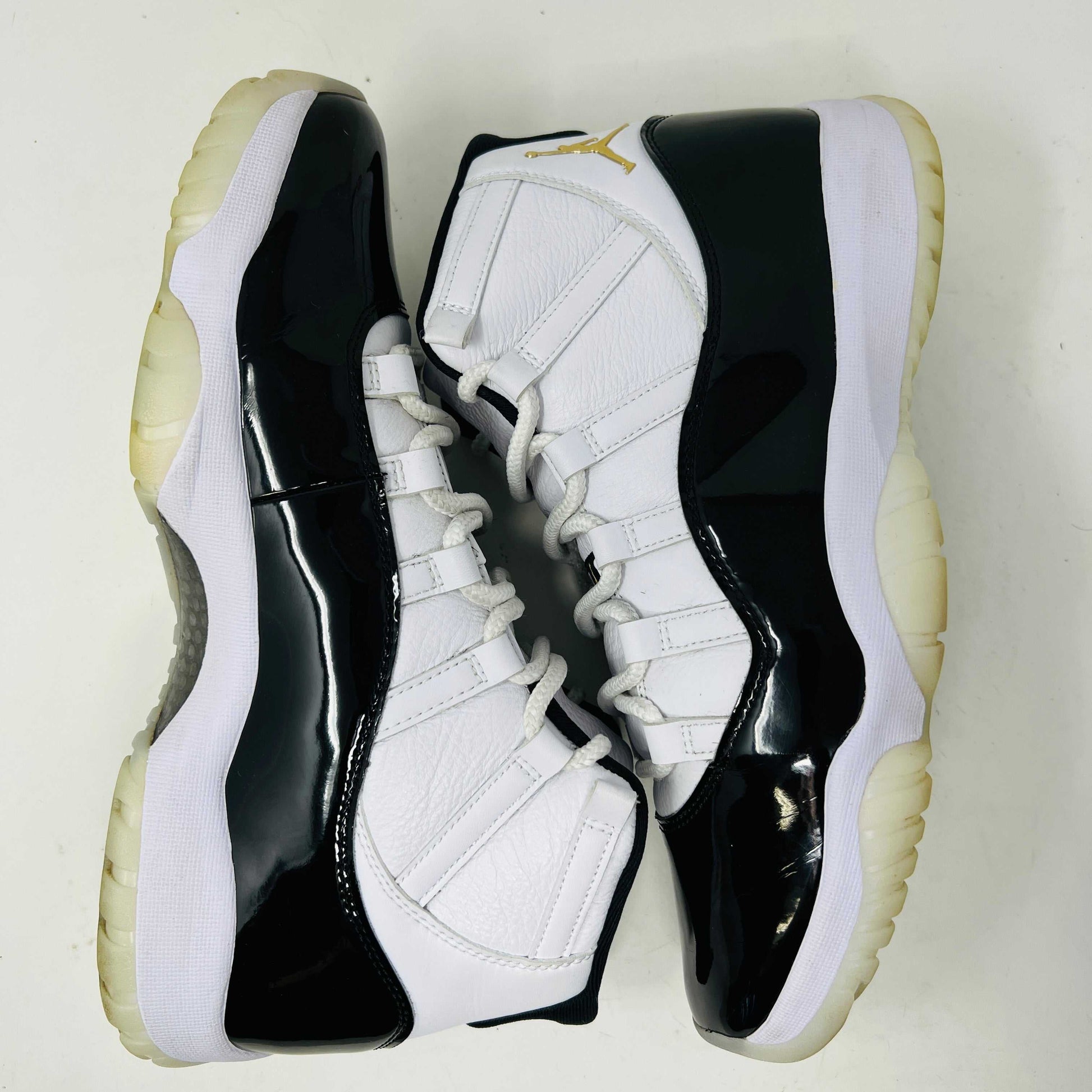 The Jordan 11 Retro DMP Gratitude (2023) sneaker, featuring white mesh, black patent leather, a translucent sole, and a gold Jumpman logo on the heel, rests elegantly on its box labeled with size and model details.